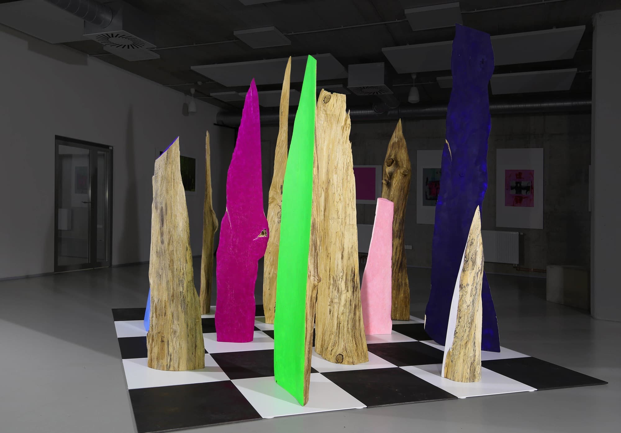 12, installation of carved wooden and colour-painted forms on a black-and-white chequered floor in a gallery