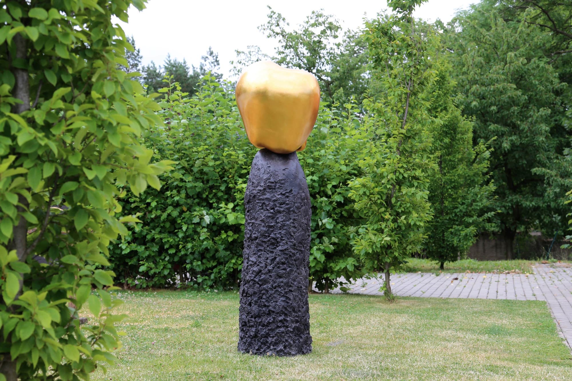 Eden, golden rounded form on a dark textured column in a garden