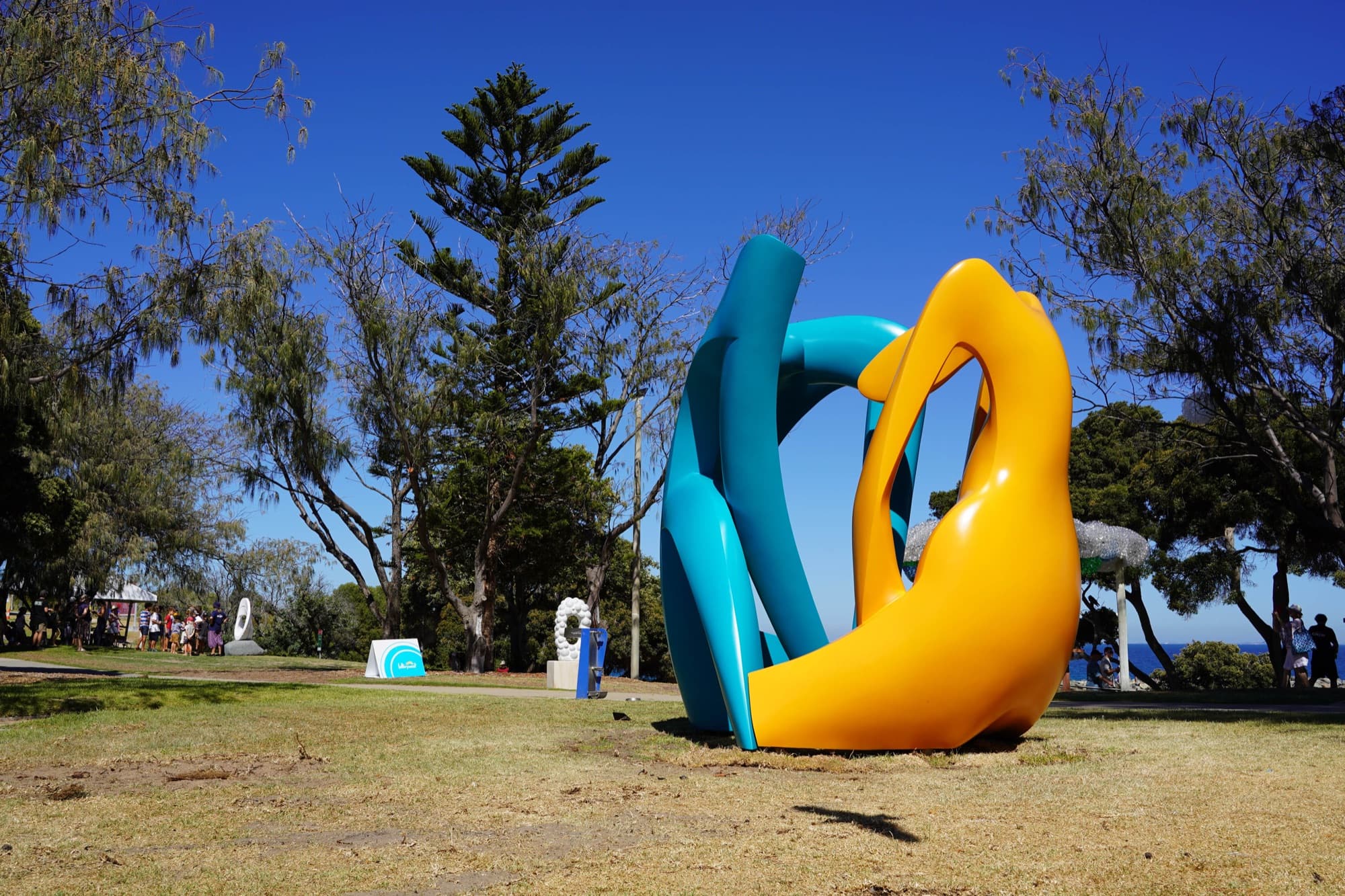 Family Natan, teal and yellow abstract forms on a seaside lawn under blue sky