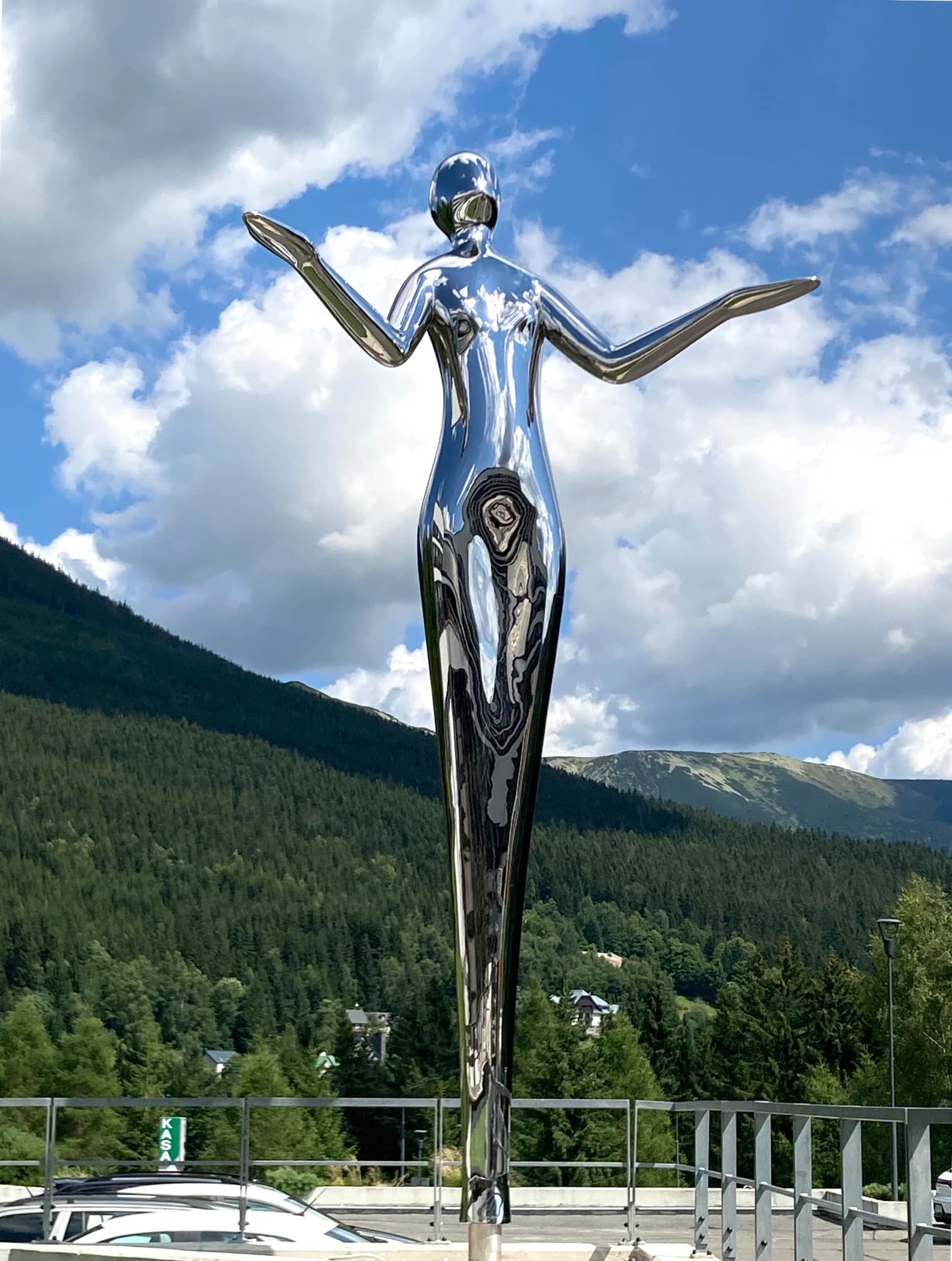 Harmony, polished stainless steel figure with outstretched arms against clouds and mountains