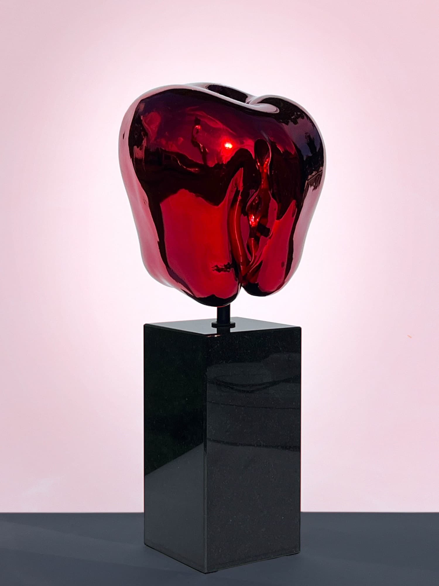 Jablko, red mirror-polished apple on a black plinth, studio photograph