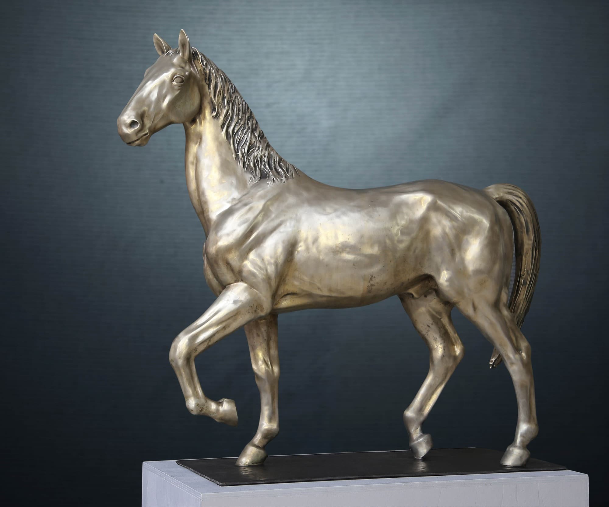 White Horse, silvery cast horse walking, side view on a plinth against a dark backdrop