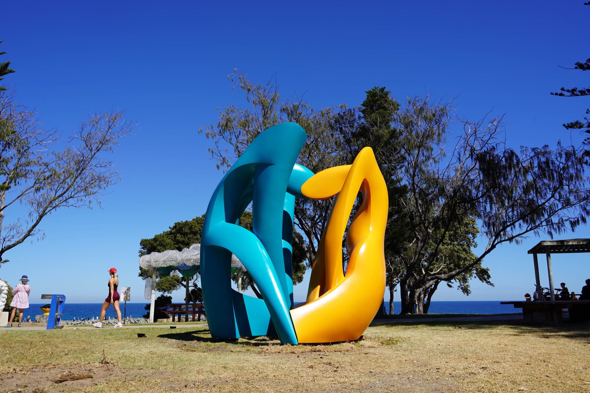 Family Natan, teal and yellow sculpture by the sea, side view
